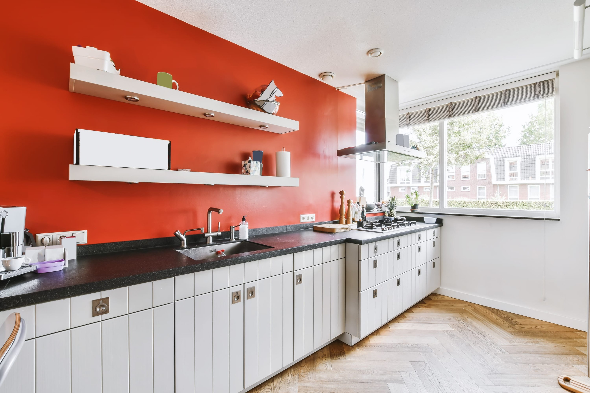 A delightful kitchen with a red wall and a white kitchen set with a black countertop