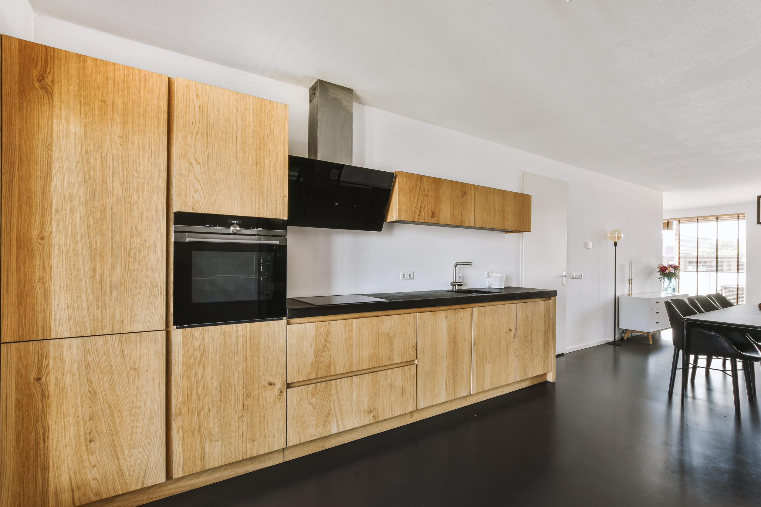 Contemporary minimalist style interior design of light studio apartment with wooden table and chairs in dining zone between open kitchen and living room with white walls and parquet floor
